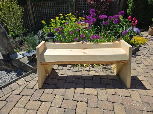 Natural wooden patio bench surrounded by vibrant flowers in a garden setting.