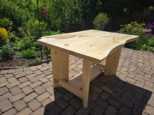 Wooden table with a natural edge, placed in a garden setting with flowers and greenery.