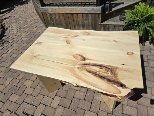A wooden table with a natural edge and visible grain patterns, placed outdoors.