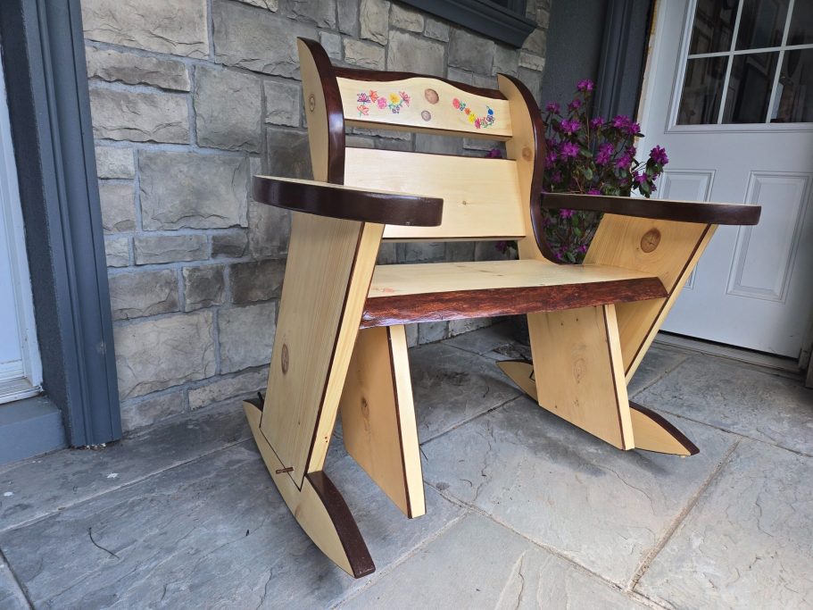 Wooden rocking chair with decorative handpainted flowers on the backrest, positioned against a stone wall.